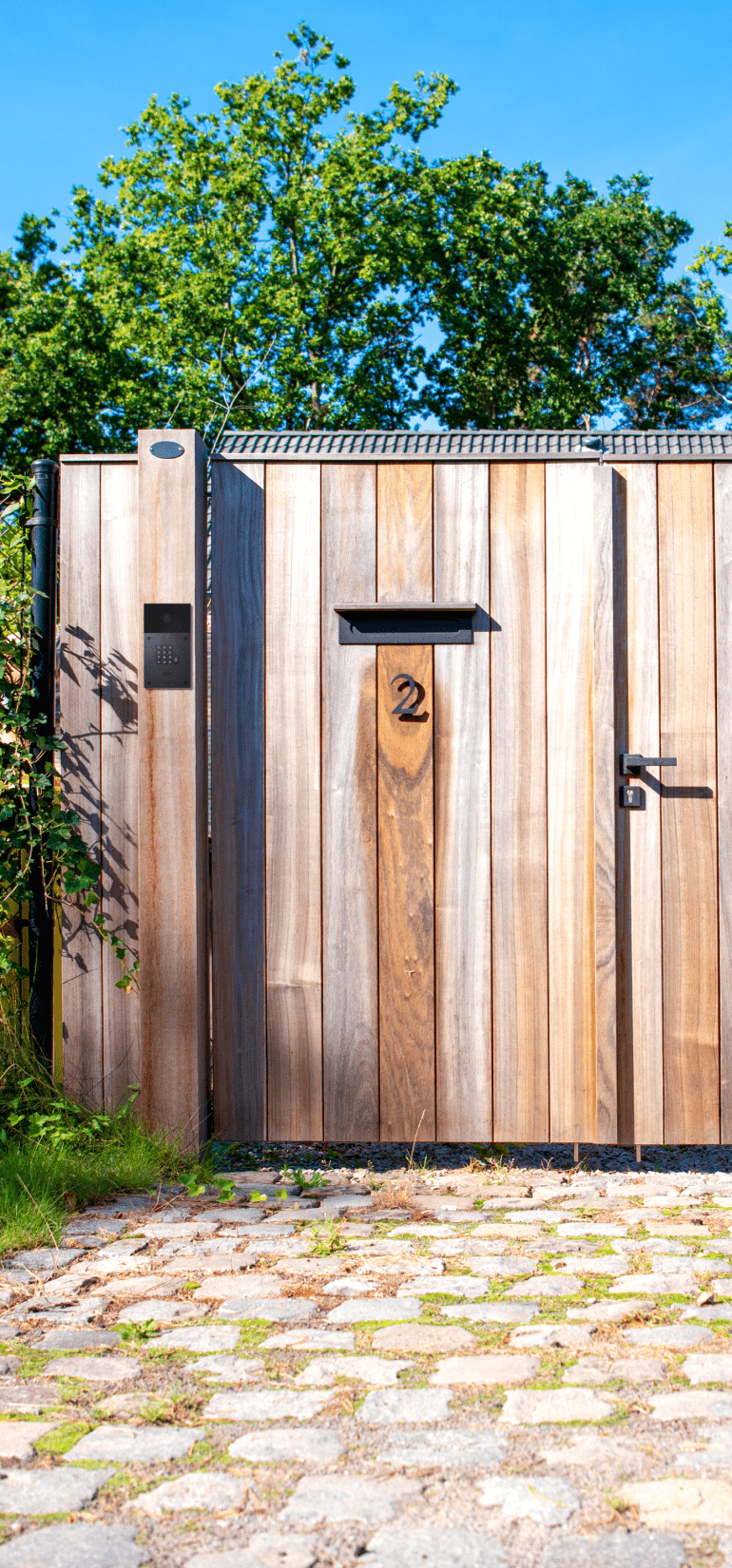 A wooden garden door with an intercom system and an integrated mail box and house number