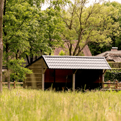 Een dubbele houten schuilstal voor paarden met zwarte dakpannen
