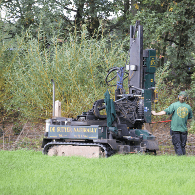 A man installs wooden fences with a post vibratory machine