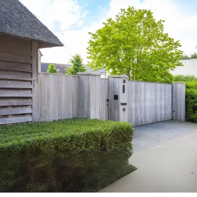 A sliding wooden gate for residential properties with vertical boards next next to a door with an intercom system