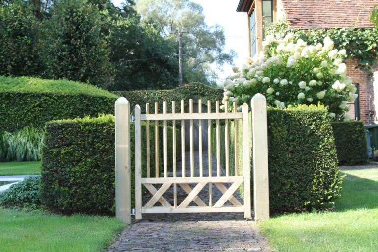 Een houten poort en een stenen looppad in het midden van een tuin en een huis en bomen aan de achterkant.