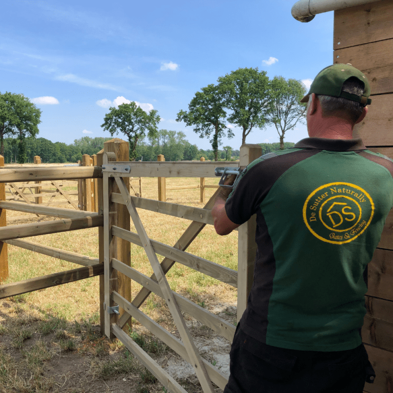 Un installateur fixe un portail de champ en bois relié à une clôture avec des poteaux carrés.