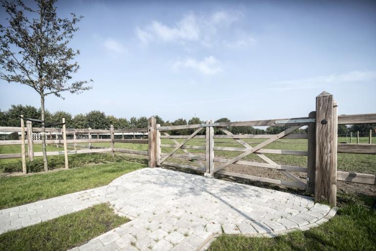 Een dubbele houten poort bevestigd aan houten omheiningen die een veld omheinen