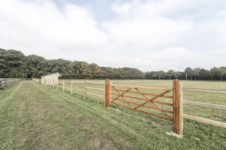 Een houten poort bevestigd aan houten omheining op een veld met een houten schuilstal voor dieren