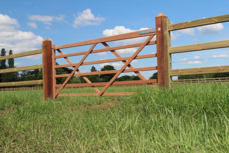 Een houten poort bevestigd aan houten omheiningen als toegang tot een veld