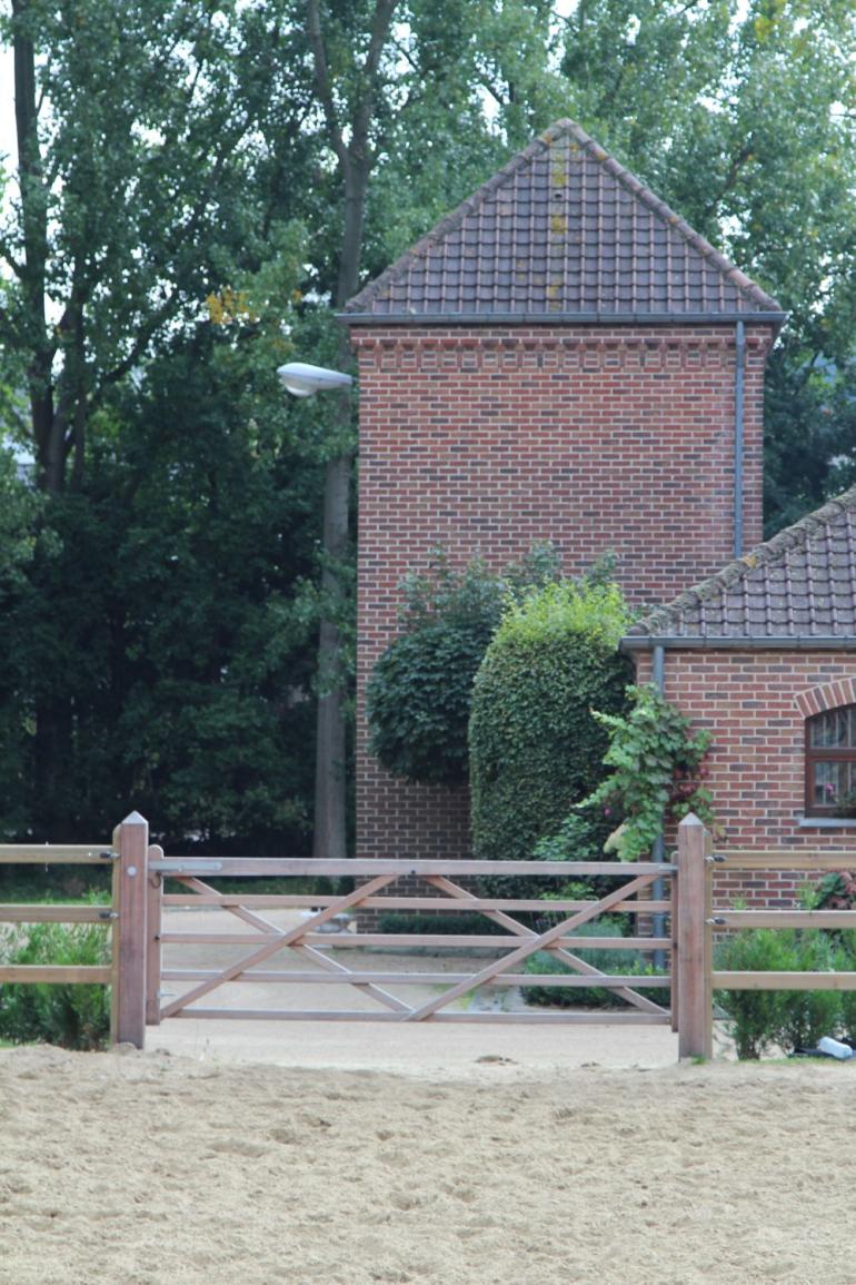 Een houten poort bevestigd aan houten omheiningen als toegang tot een rijbak