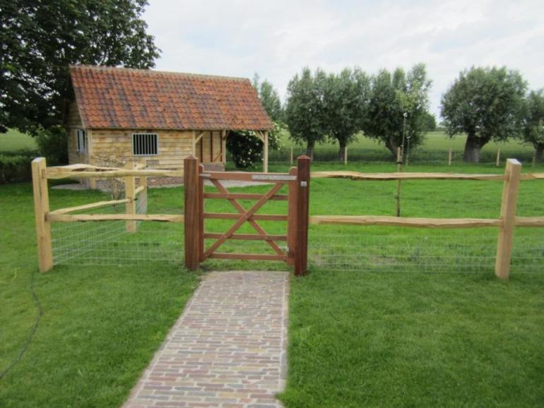 Een houten poort bevestigd aan een rustiek houten omheining die een tuin omheint