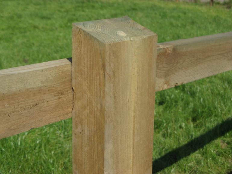 Een houten plank vastgeschroefd aan een houten vierkante paal van een omheining