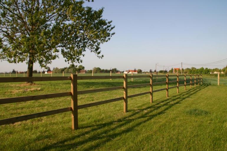 Een houten omheining op een veld met de planken vastgeschroefd aan de palen