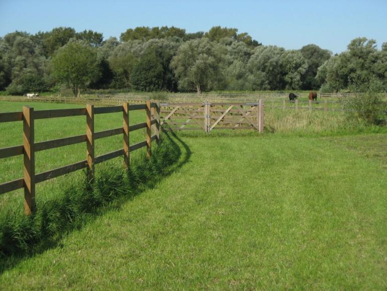 Een houten omheining op een veld met de planken vastgeschroefd aan de palen en een houten veldpoort