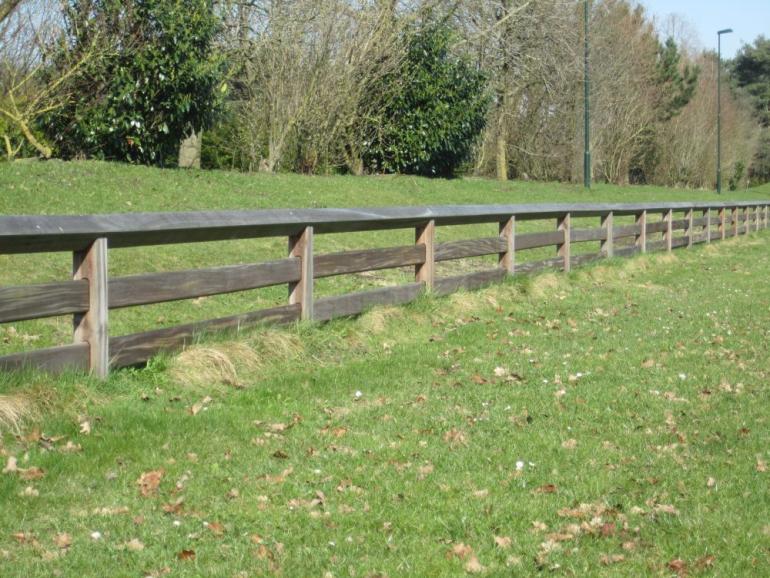Een houten omheining met 2 rails, planken die door de palen glijden en een doorlopende bovenrail