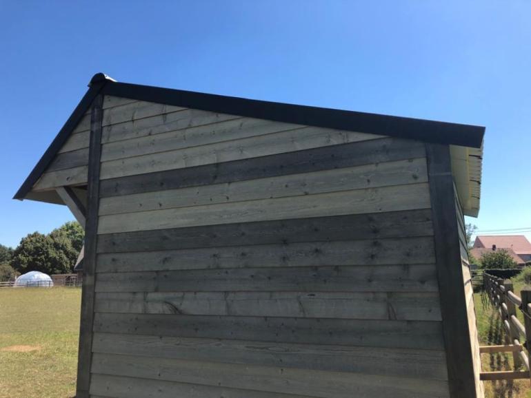 Het zijaanzicht van een houten schuilstal voor buitendieren met zwarte dakpannen