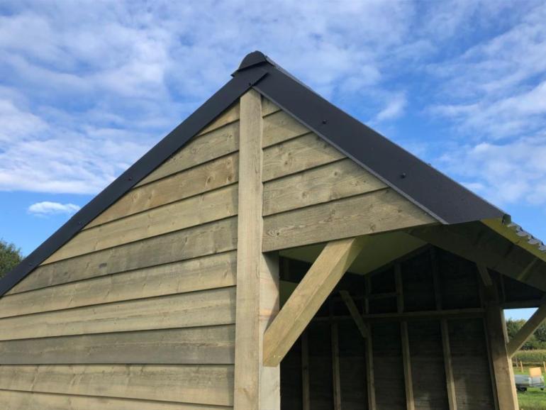 Het dak van een houten schuilstal voor buitendieren met zwarte dakpannen