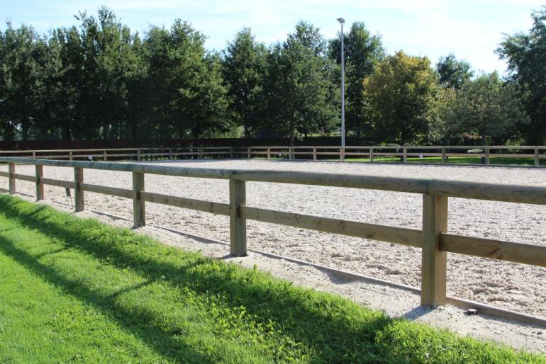 Een paardrijbak omheind met houten omheiningen met één rail, vierkante palen en een doorlopende bovenrail