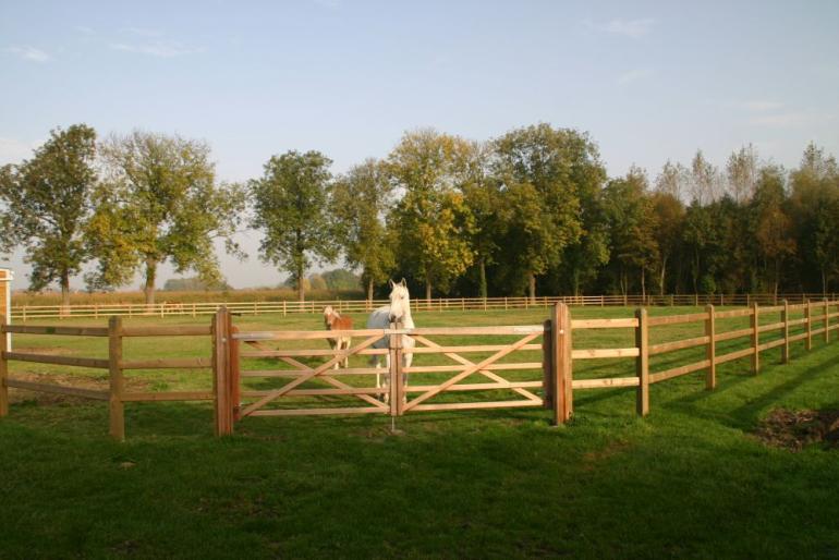 Een dubbele houten veldpoort bevestigd aan houten omheiningen met drie rails en vierkante palen