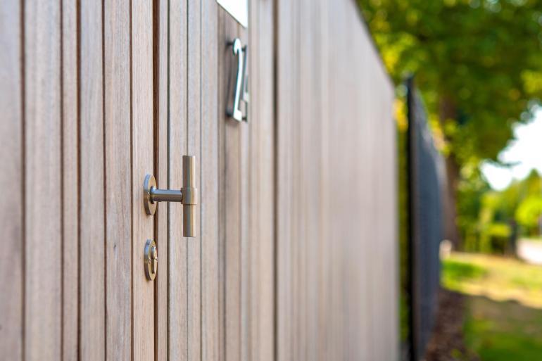 Une poignée de porte et un numéro de maison attachés à une porte de jardin en bois