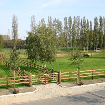 Un double portail en bois donne accès à un chemin bordé de nombreux champs clôturés par des barrières en bois de 3 lisses.