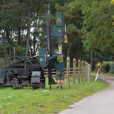 Un homme installe des clôtures en bois à l'aide d'une machine à vibrer les poteaux.