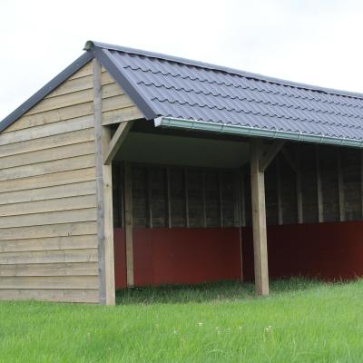 Een dubbele houten schuilstal voor paarden en buitendieren met zwarte dakpannen