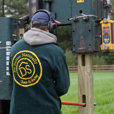 A man installs wooden fences with a post vibratory machine