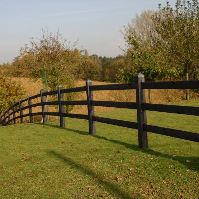 Une clôture en bois noir avec des poteaux carrés et 3 lisses sur un champ