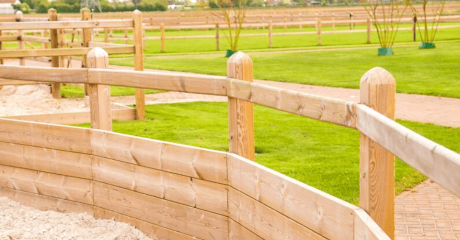 Un rond de longe clôturé par des barrières en bois avec des poteaux carrés, 1 lisse et des planches de gravier au fond.