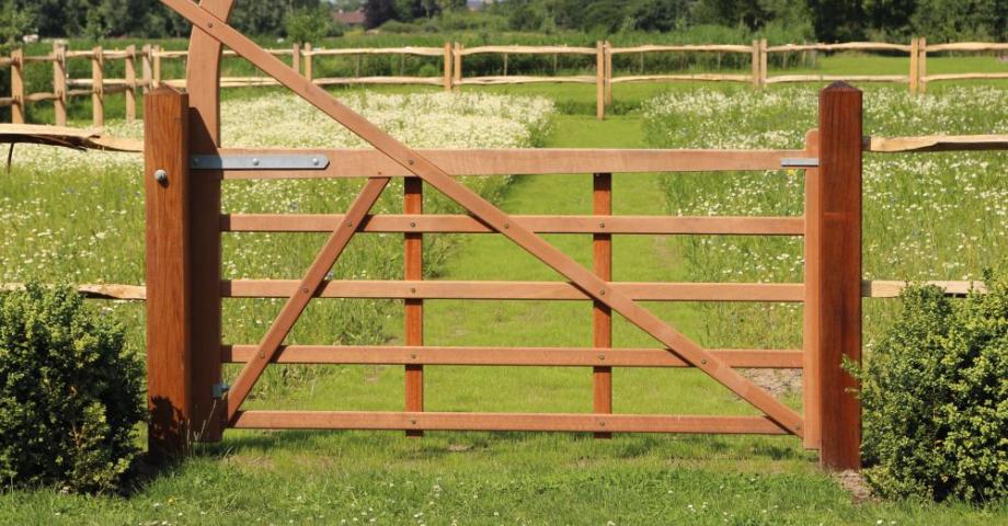Un portail de champ en bois avec une arche reliée à une clôture en bois.