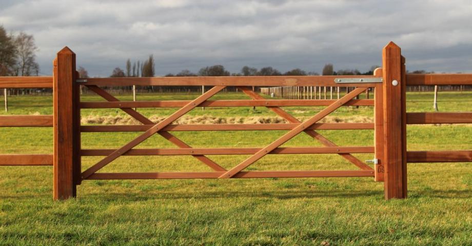 Houten poort bevestigd aan houten omheiningen, gebruikt als toegang tot een veld.