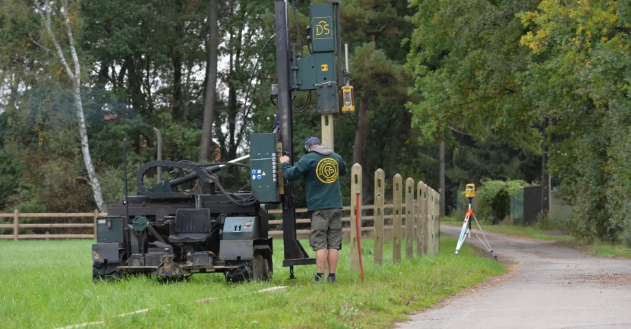 A man installs wooden fences with a post vibratory machine