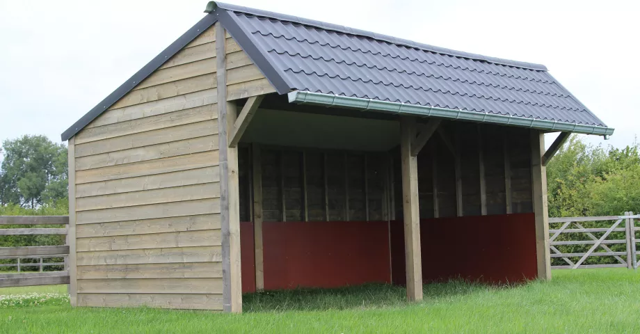 A double wooden shelter for horses and outdoor animals with black roof tiles