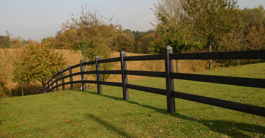 A black wooden fence with square posts and 3 rails on a field