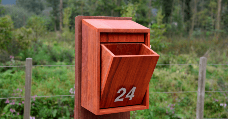 Een moderne houten brievenbus die naar voren opent en een groot huisnummer heeft 