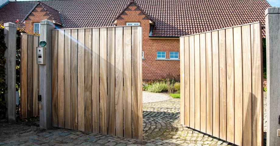 Een houten oprit draaipoort met verticale planken en een intercomsysteem