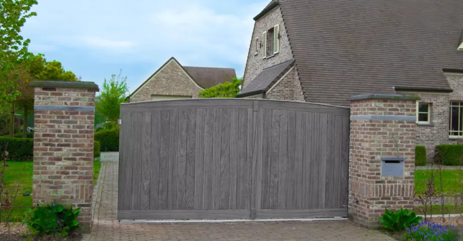 A wooden driveway swing gate with an arch next to a door with the same design and with a house number and a mailbox integrated.